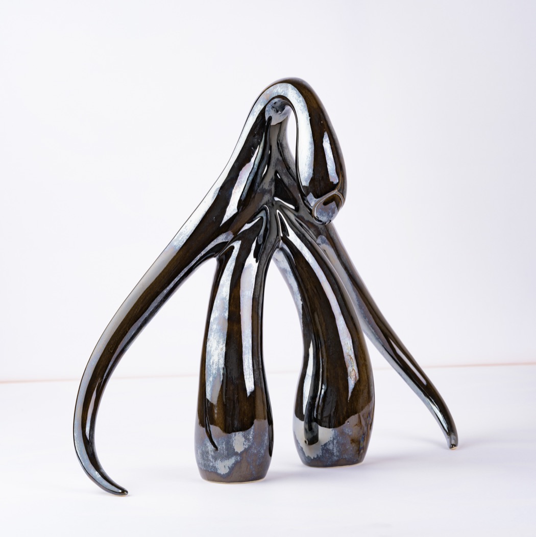 Swan Series by Sophia Wallace — a dark glazed stoneware sculpture standing on two tapering forms beneath a long curved crown, drawing on the line of a swan in motion.