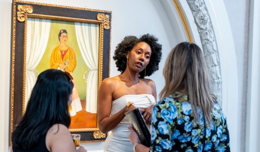 Guests at a past Power Up opening night in conversation in front of a framed portrait painting